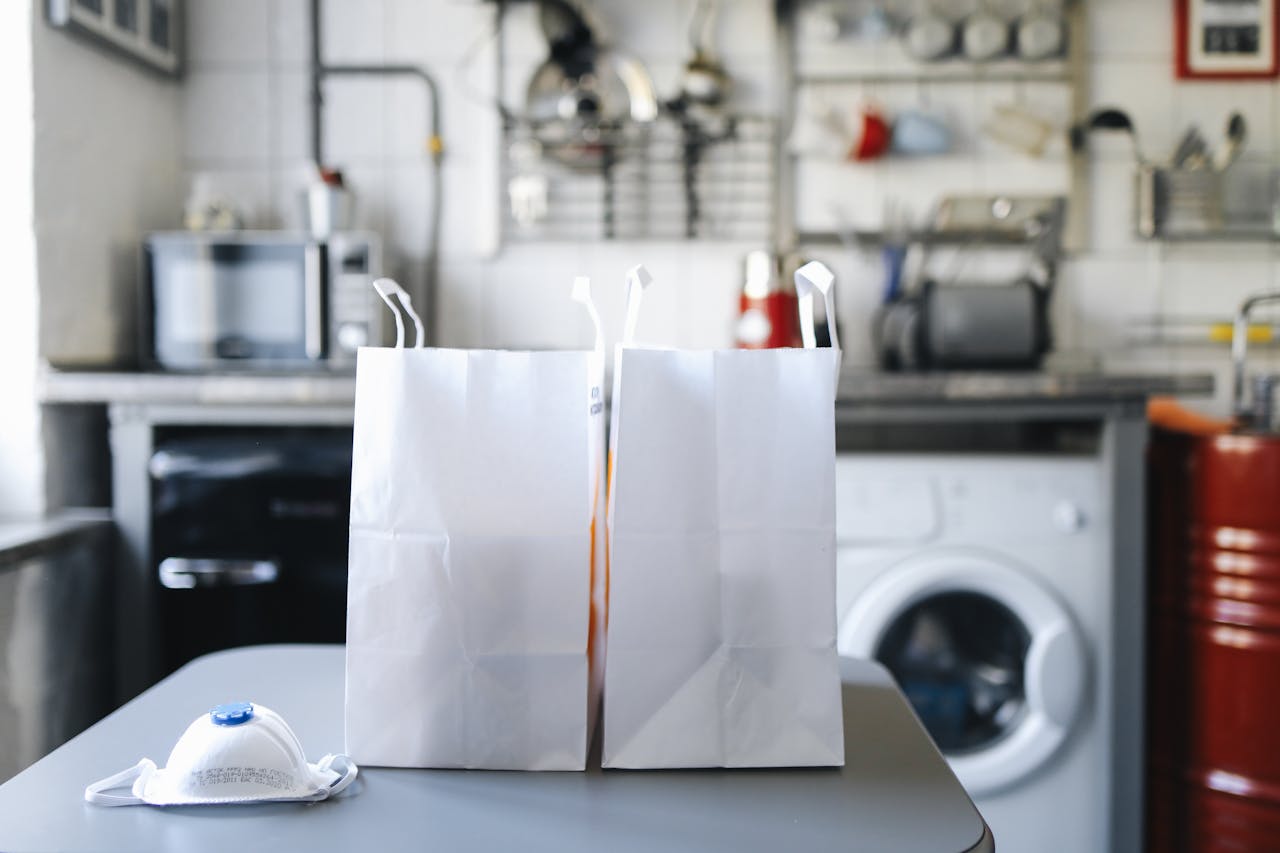 services-02 Modern kitchen interior with two paper bags on a table and a facemask, emphasizing hygiene.