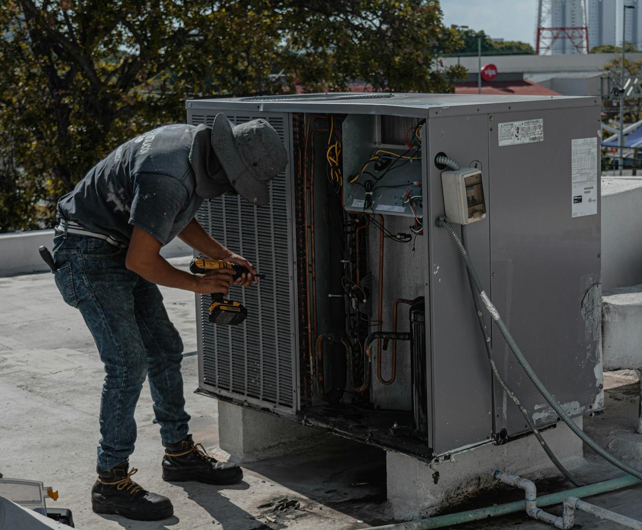 services-04 A worker in a bucket hat repairs an outdoor air conditioning unit on a rooftop.